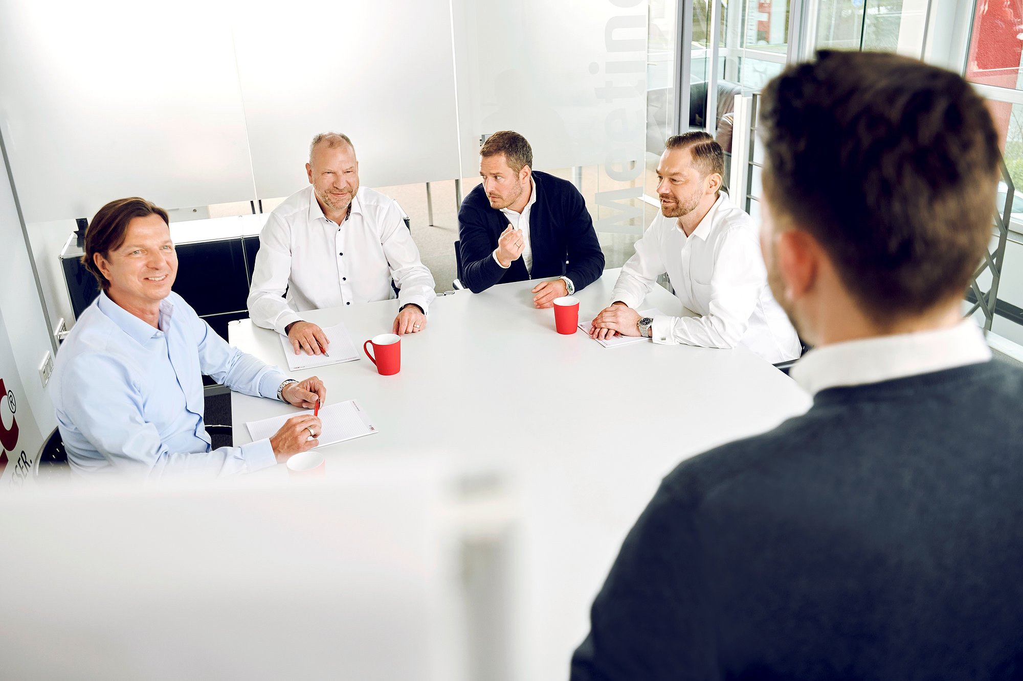 Gruppe von Personen sitzt im Besprechungsraum an einem weißen Tisch.